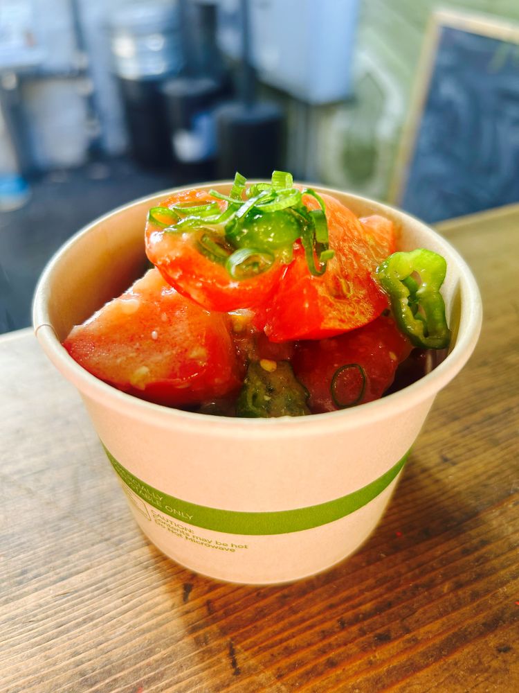 A small bowl of tomatoes and padron peppers sitting on a wooden countertop.
