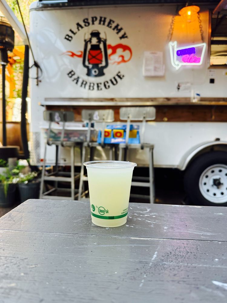 Photo of a slushy margarita on a picnic table with the blasphemy bbq bar cart behind it.