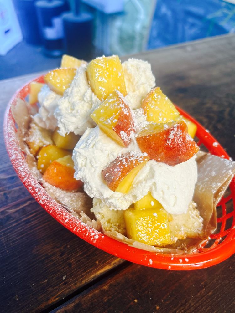 A red tray with a biscuit smothered in whipped cream, peaches, and powdered sugar sitting on a wooden counter.
