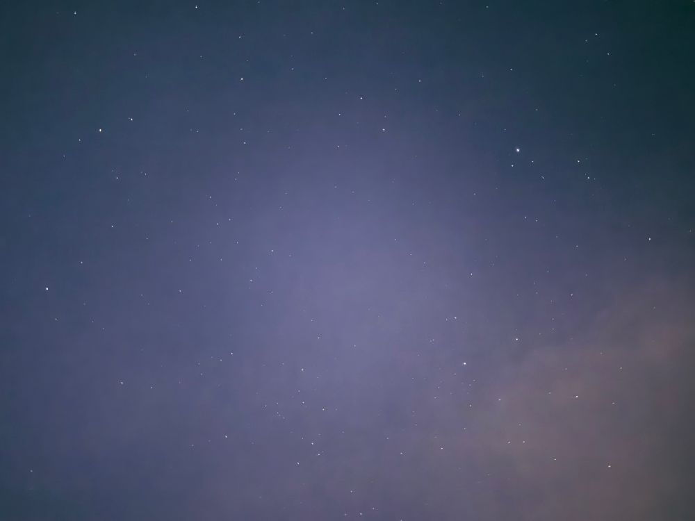 Viele funkelnde Sterne am nachtblauen Himmel. Ausschnitt der Milchstraße, die als feiner dunkelrose- und zartviolettfarben „Wolken“ zu erkennen ist. 