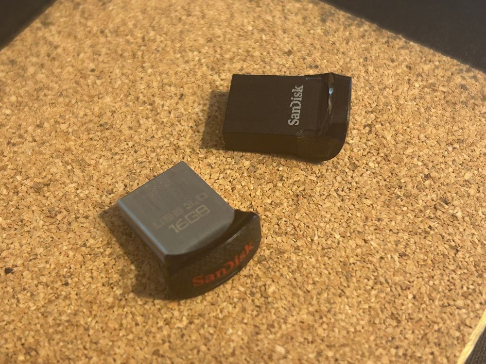 2 Sandisk thumb drives. Old one robust metal construction. New looks to be made of bendy cardboard