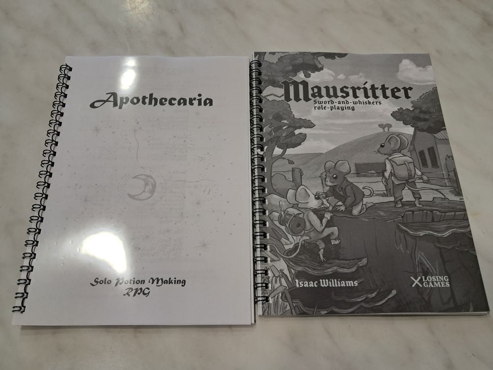 A couple of black and white printed TTRPGs: Apothecaria and Mausritter.