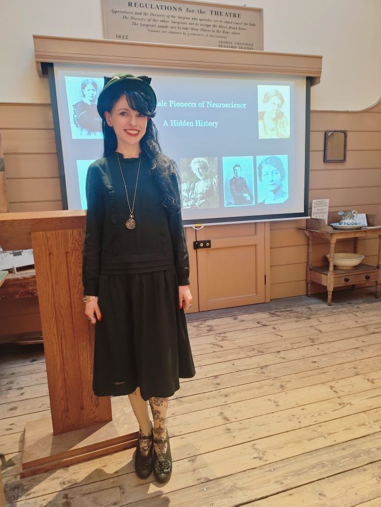 Female scientist in front of slide displaying some of the female pioneers of neuroscience 