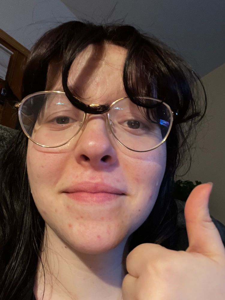 a woman with dark hair and glasses crying and giving a thumbs up