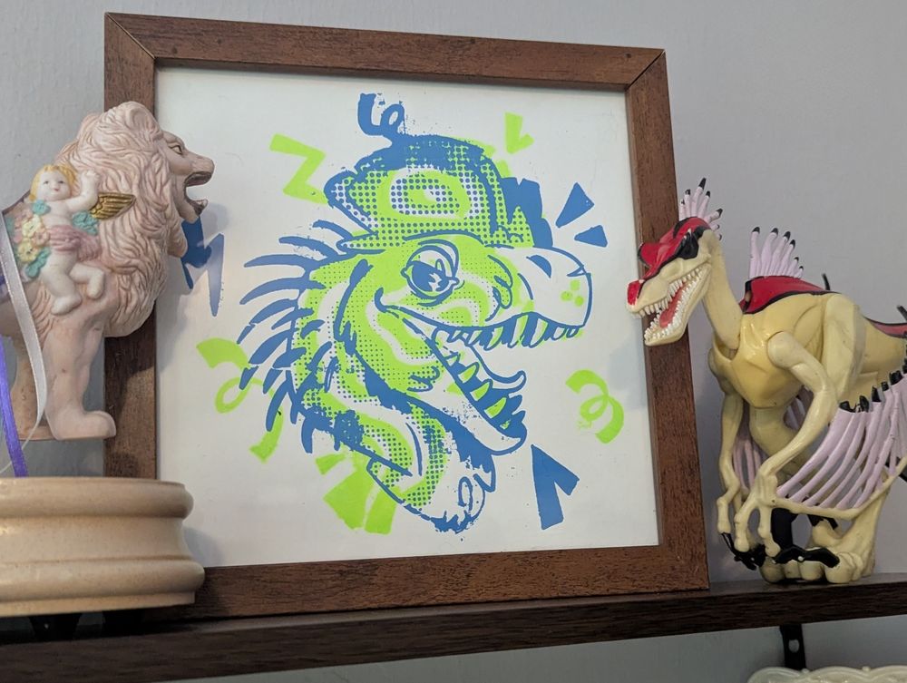 a framed screen print of a neon green and blue dilophosaurus bust on a shelf between a carousel lion and a well loved Jurassic Park chaos effect figure