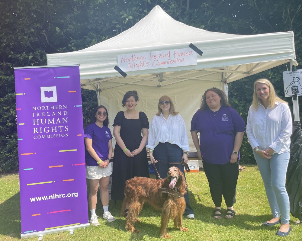 Five people stand under a gazebo with a purple NIHRC sign to the left, and a red setter dog in front. 