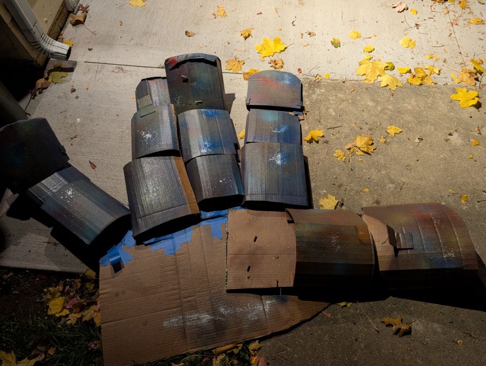 A view of the "hand" with the palm facing up. The segments of the cardboard fingers can be seen as discrete pieces of cardboard that have been curved and attached to a flat piece of cardboard.  Everything looks flatter because the cardboard has spent time out in the elements.  A downspout from a home's gutters is in the corner of the picture and looks small in comparison.