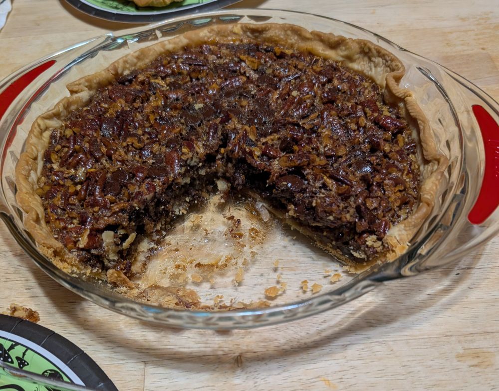 In a glass pie pan is a one-crust pie made with pecans, chocolate chips, and bourbon plus all the other pecan pie ingredients.  There is a large wedge missing because two slices have been cut out and served.