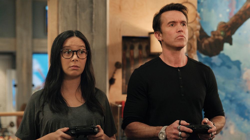 Ian and Poppy hold video game controllers and stare in awe off screen.