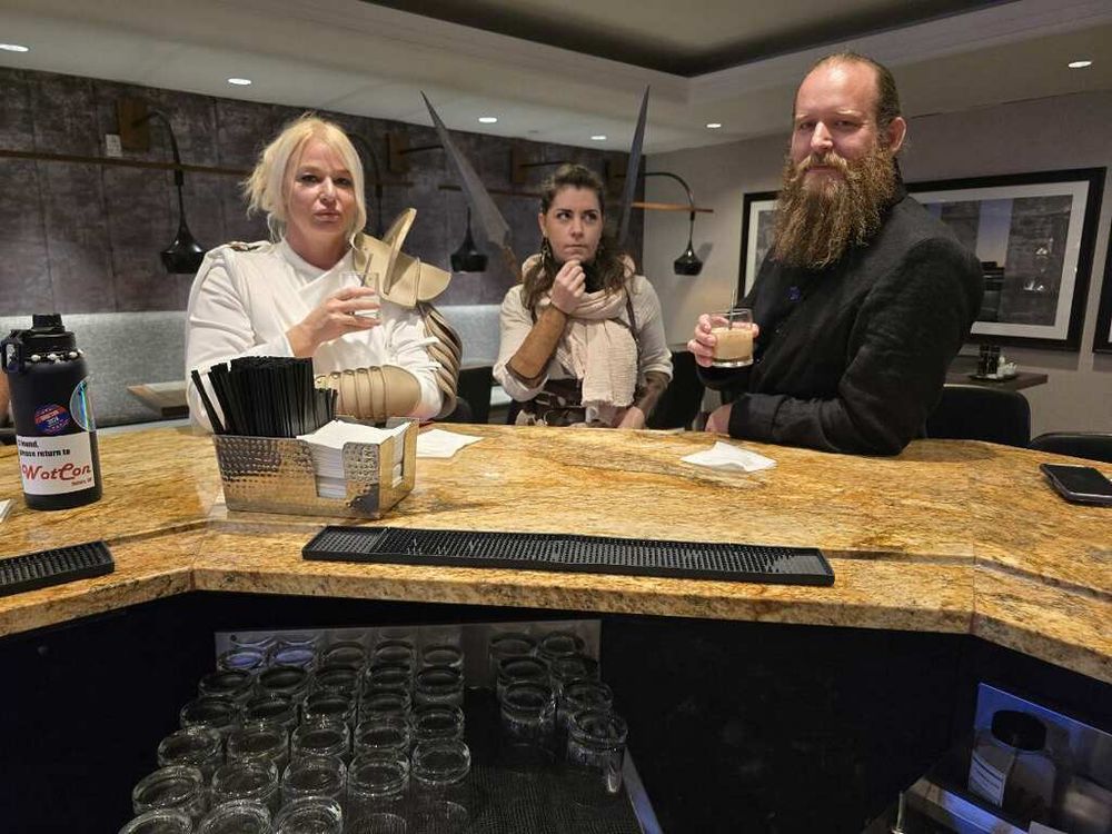 London River and White cloak cosplay A woman in the middle dressed like a maiden of the sphere, and a man on the right of the image wearing a black coat f an ashaman 