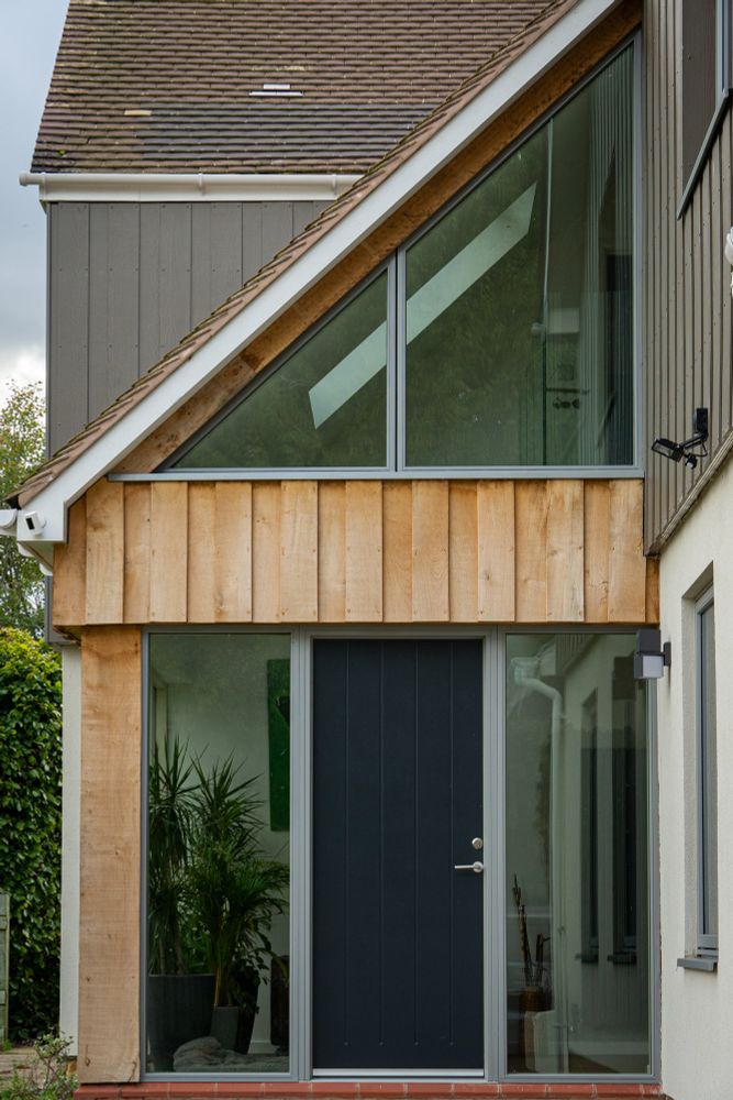 Triangular glazed window over RAL 7016 panelled entrance door with sidelights; Frames coloured GRIS 2150
