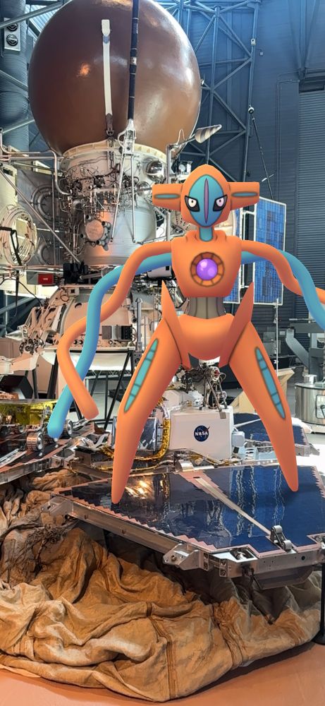 Deoxys, an orange-and-teal DNA alien Pokémon, stands atop the outstretched solar panel of the prototype Mars rover (Sojourner/Pathfinder) on display at the National Air & Space Museum’s Udvar-Hazy Center.
