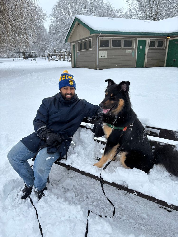 man with dog sitting on a park bench in the snow. the dogs eyes are closed with his tongue hanging out 
