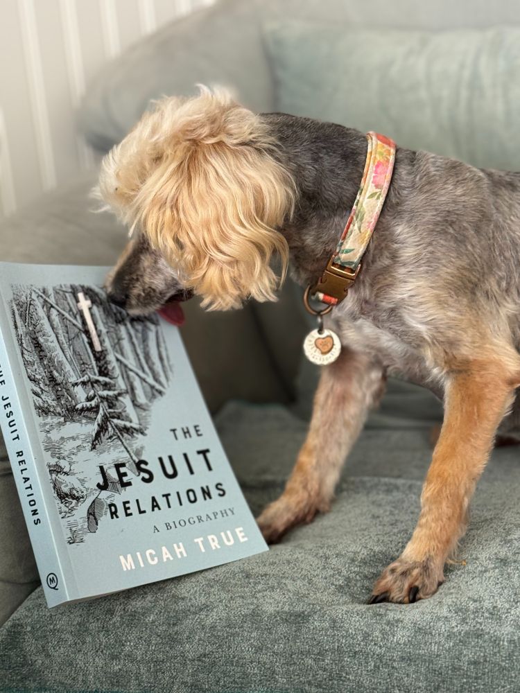 small dog licking a book entitled "The Jesuit Relations a Biography" by Micah True