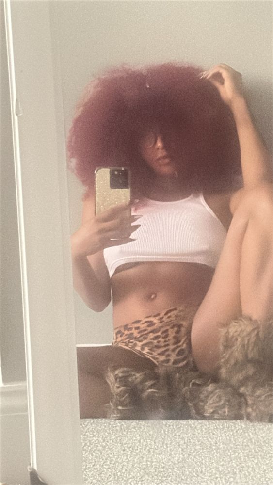 Curly red headed Black woman wearing fur leg warmers animal print bottoms and white baby tee with glasses