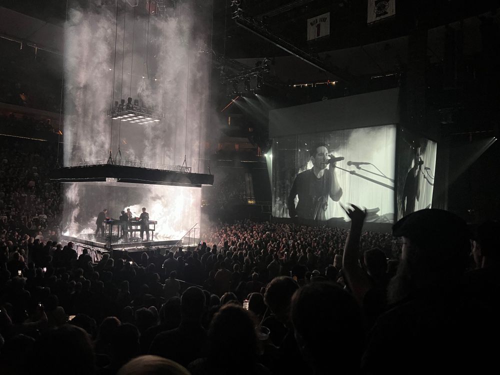 Nine Inch Nails and Boys Noize perform on a secondary stage in the middle of Xcel Energy Center while a close up of Trent Reznor is projected on fabric in front of the main stage.