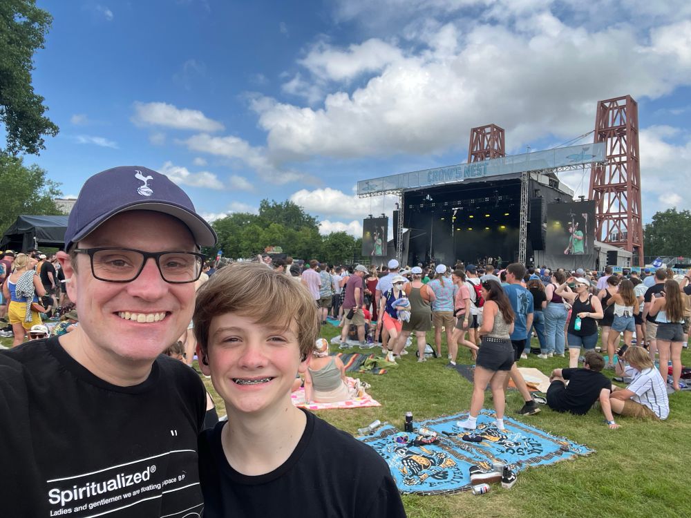 A proud dad and his son at an outdoor festival stage. Dad is wearing a Spurs hat and a Spiritualized shirt.