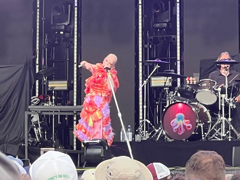 Shirley Manson of Garbage showing she’s still an absolute rock star while wearing an absurd red, purple, yellow, and orange dress partially made of plastic on a hot and sunny day.