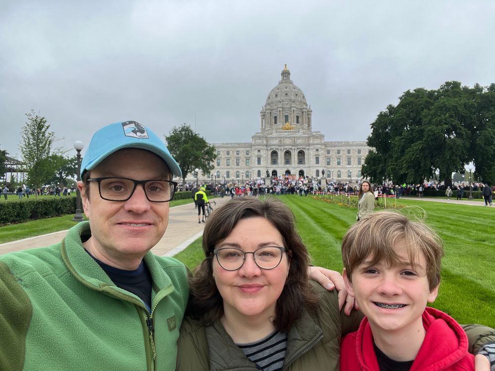 A family selfie in front of the Minnesota State Capitol where a crowd is starting to gather.