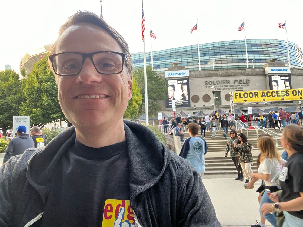 A guy in an Edge Fest 3 shirt and glasses takes a selfie outside Soldier Field where Oasis is about to play.