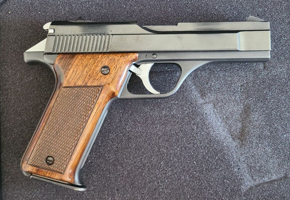 A right-side photograph of a handgun. The grips are checkered wood and the metal is a glossy gray-black. This pistol was developed and produced by Benelli in Italy in the mid 1970s for military contracts and civilian sports use. Due to mechanical complexity and other factors it was unsuccessful and only about 10,000 examples in total were produced between 1976 and 1990. 
