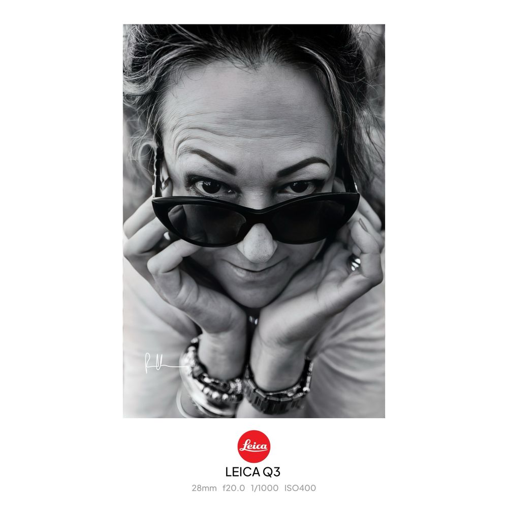 Portrait of a close up of a middle aged woman’s face cupped in her hands and looking over her sunglasses at camera 