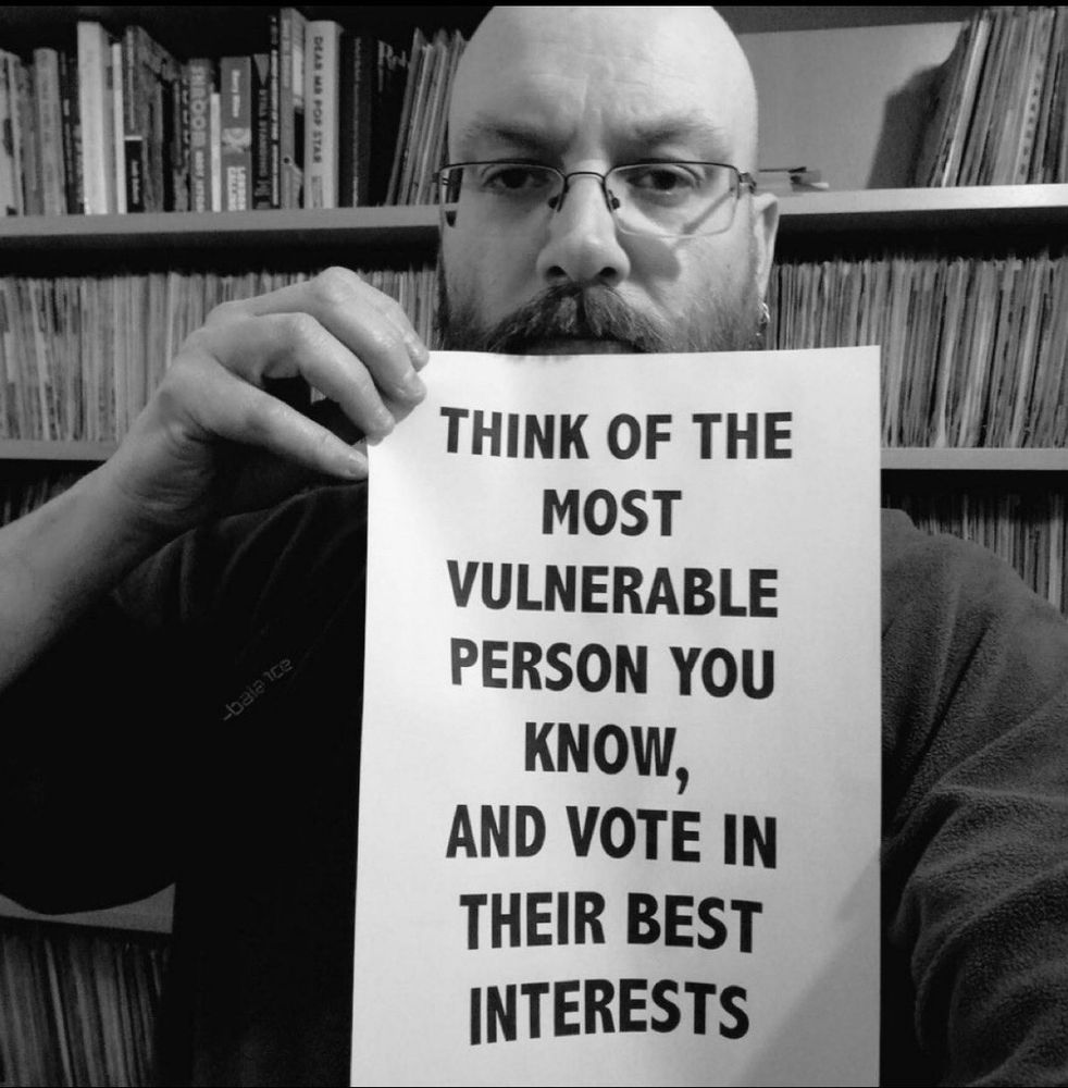 A man holding a sign saying: THINK OF THE MOST VULNERABLE PERSON YOU KNOW,
AND VOTE IN THEIR BEST INTERESTS