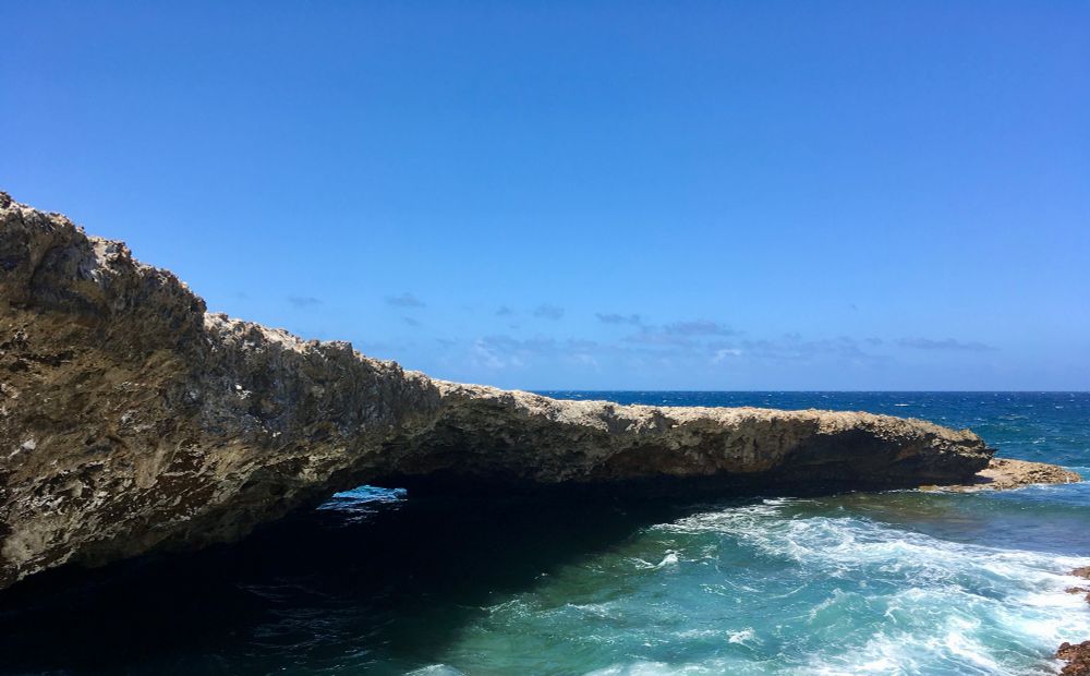 Natural bridge in Curaçao. Waves crash against a rocky, craggy outcrop that has been hollowed out by erosion to form a natural bridge.