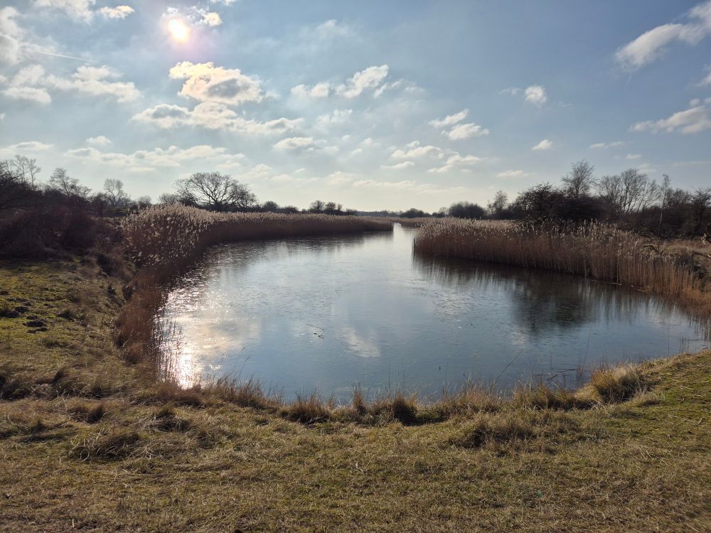 Watergang in de duinen. De lucht spiegelt in het vlakke water.