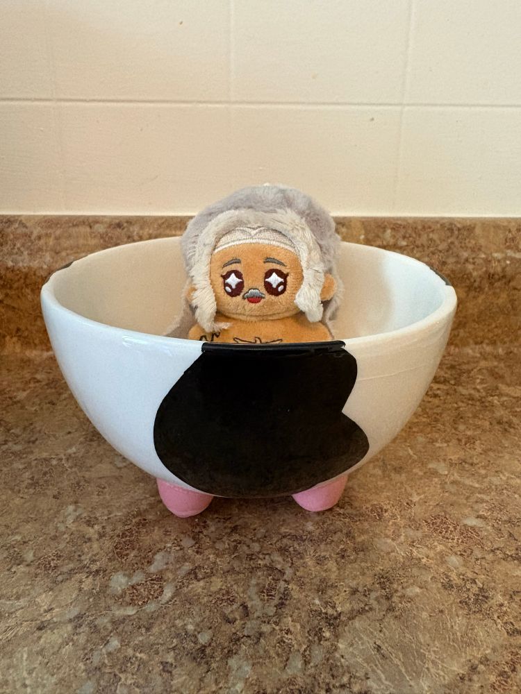 A 5cm Ed doll by rights, naked, in a bowl with cow print with pink legs that look like udders.