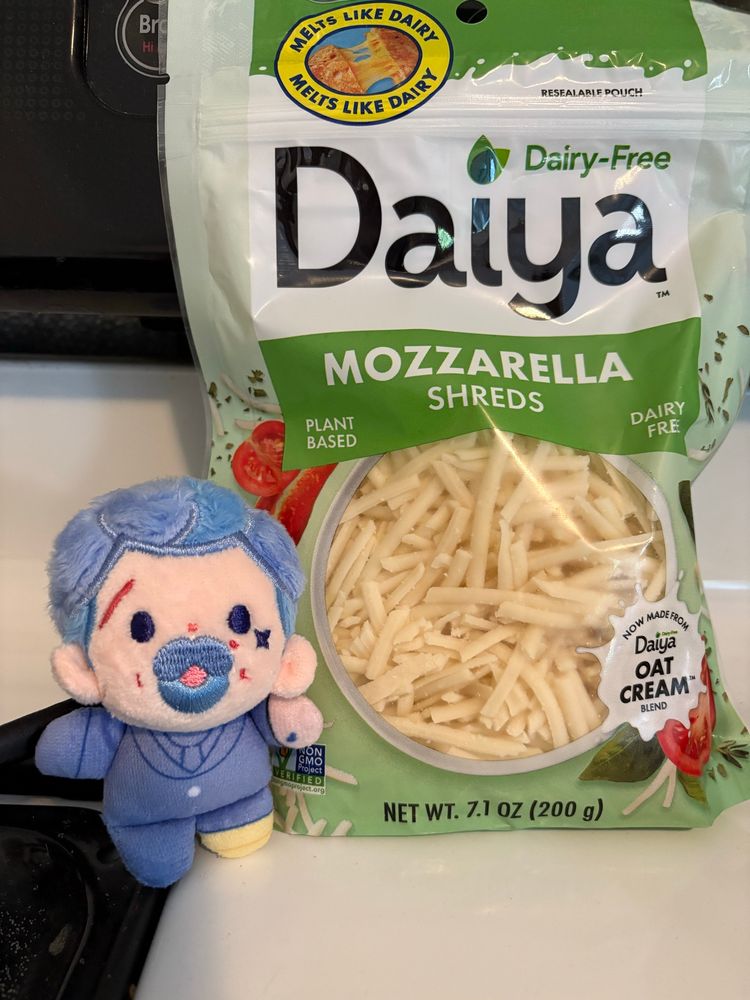A 5 cm Izzy doll by rights next to a bag of Daiya dairy free mozzarella shredded “cheese” 