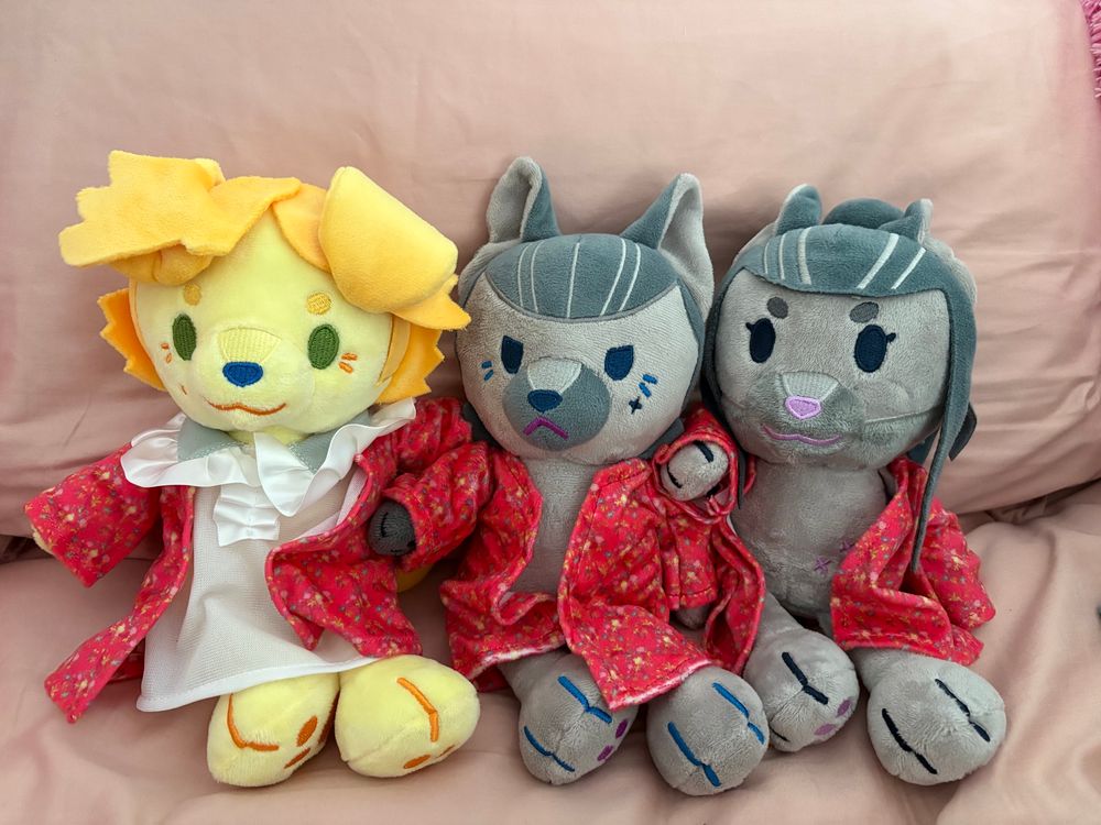 animal dolls of Stede as a dog, Izzy as a dog, and Ed as a wolf (I think) in matching red depression robes. Stede also has a night gown under his robe. They’re lined up sitting next to each other against a pink pillow. Dolls by Babirousa! They’re very cute 