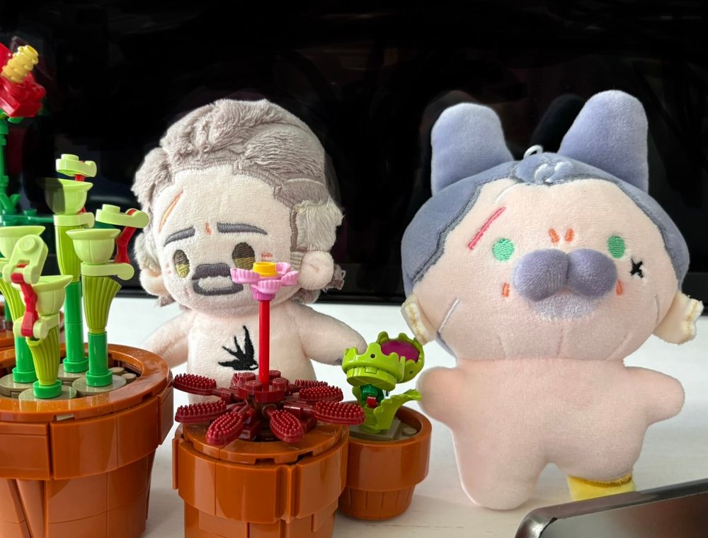 A naked Izzy doll by rights being partially blocked by Lego flowers including a tiny Venus fly trap and pitcher plants , next to a naked Izzy bunny doll also by rights that is not blocked. They’re really cute. They’re leaning against a tv that I badly tried to erase the reflection of. 