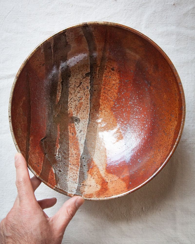 A vermillion orange-red, white and black organically decorated large ceramic bowl. A hand is reaching for the bowl, showing scale. 