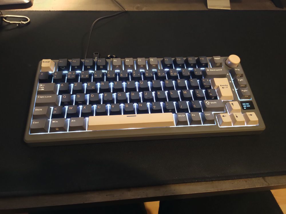 Clavier 75% gris, beige et noir avec un rétro-éclairage blanc sur un tapis de souris noir