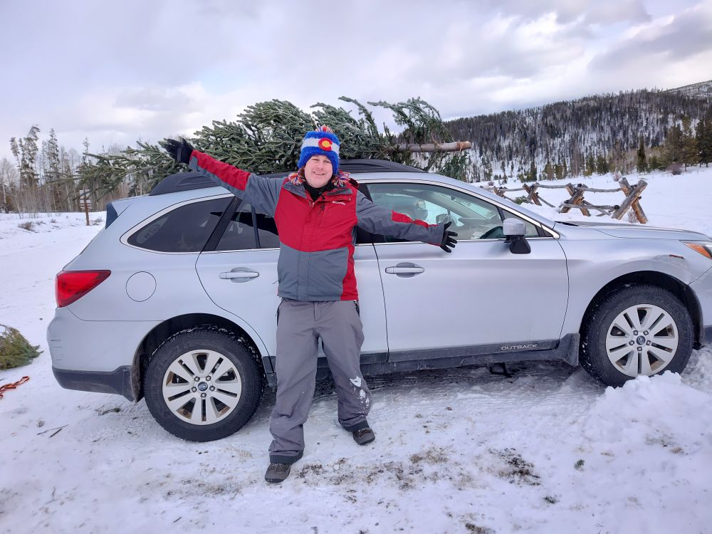 A pale white person standing in front of the car with a tree lashed to the top