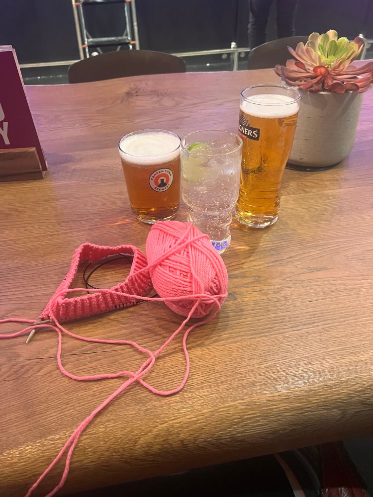 Several alcoholic drinks, including a cider, are shown next to a knitting project