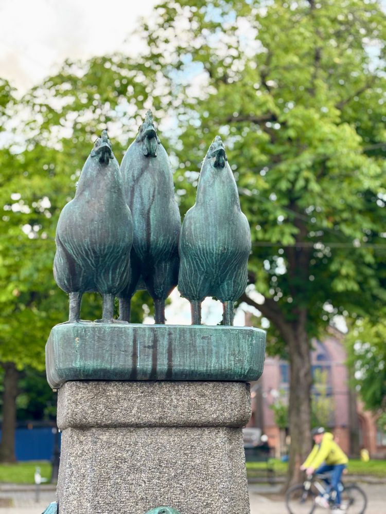 A bronze statue of one rooster and two hens facing forward.