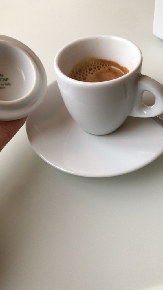 A “caffe lungo” served in a white cup with matching saucer, held next to its lid.