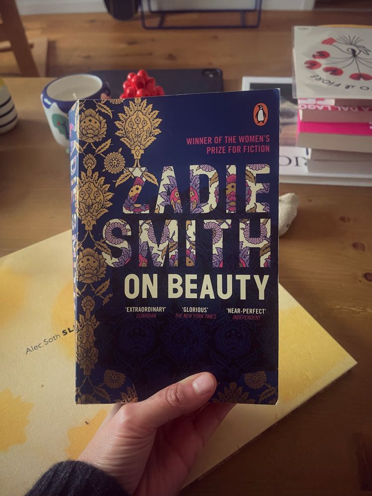 A hand holding the book “On Beauty” by Zadie Smith with a patterned cover.