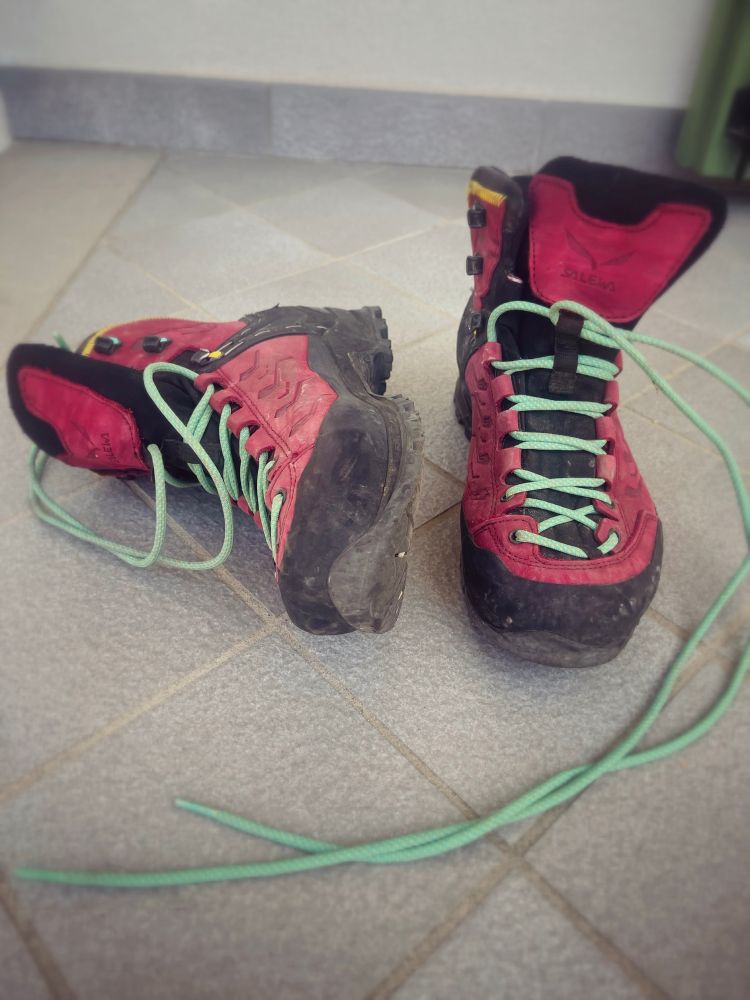 A pair of worn red hiking boots with light green laces. The boots show signs of use: they have been used a lot on mountain trails.