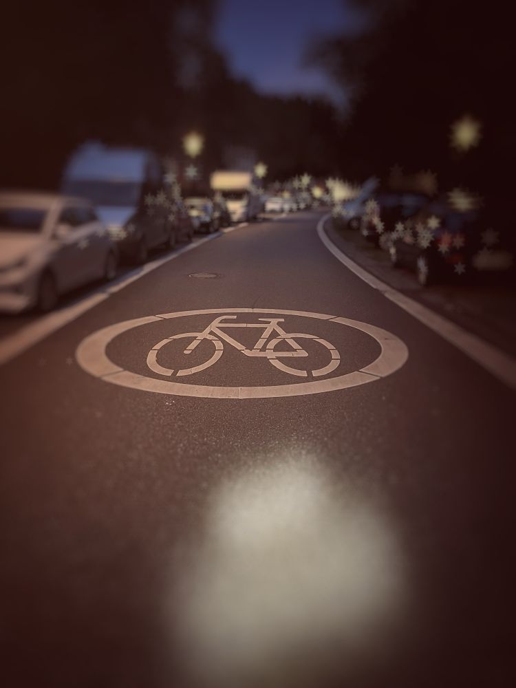 Night view of a quiet urban street with a large bicycle symbol painted on the asphalt, indicating bike priority. It shows a calm and safe atmosphere for cyclists ♥️