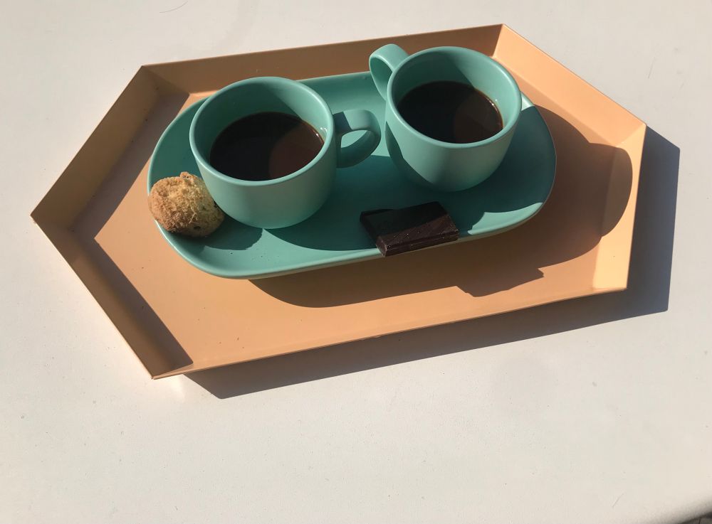 Two blue coffee cups on a peach-colored tray, served with a cookie and a piece of dark chocolate