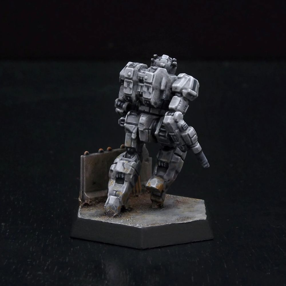 A rear view of a painted miniature of a Wasp 'Mech.  It is light ash gray, and the cockpit glass is dark red.  It is posed as if dashing.  It is next to a knee-high gray concrete wall.  Thin black stripes decorate its shoulders. 
