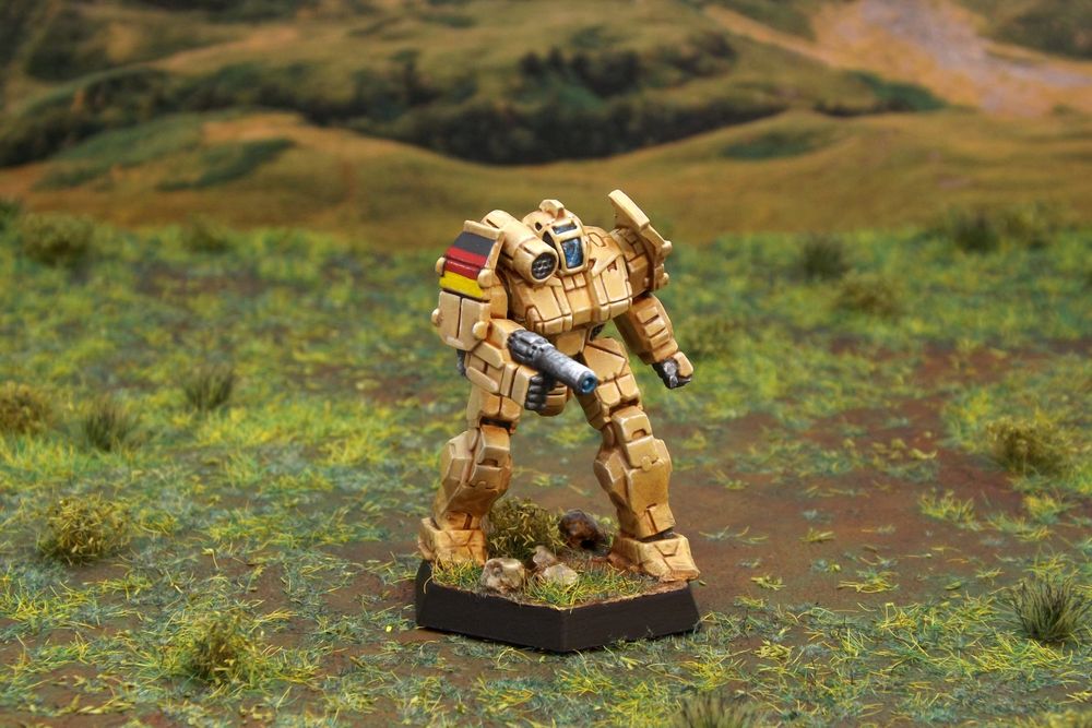 A painted miniature of a Griffin 'Mech.  It is tan and the cockpit glass is blue.  The right pauldron has three horizontal stripes: black, red, and gold.  The miniature is photographed on grassy terrain.