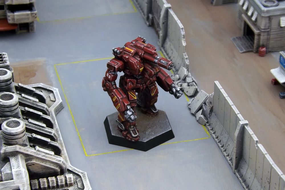 A painted miniature of a Legionnaire 'Mech.  It is dark red with yellow stripe highlights.  The number "55" is on the right upper arm.  The miniature is photographed in an urban scene.