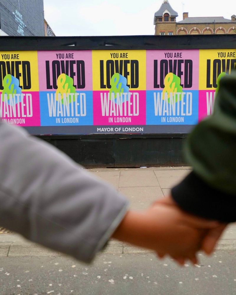 Two people holding hands in front of Loved & Wanted billboard posters