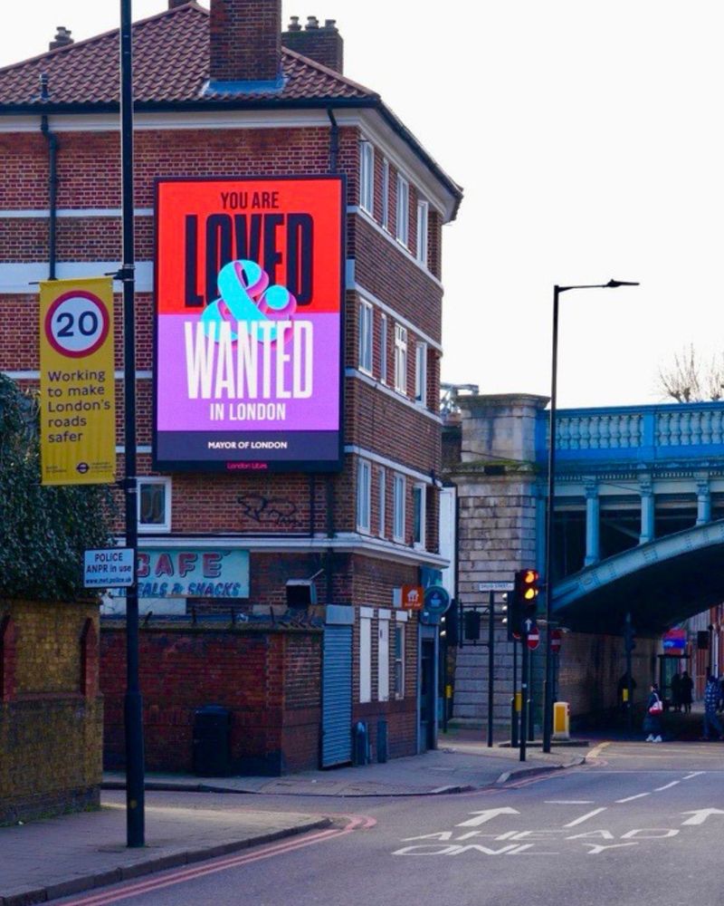 A Loved & Wanted poster on the side of a café, next to a railway bridge