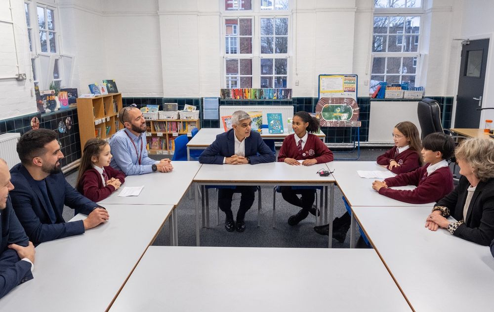 Mayor of London Sadiq Khan seated at a table, engaging in a discussion with staff and students of Avondale Park Primary School.