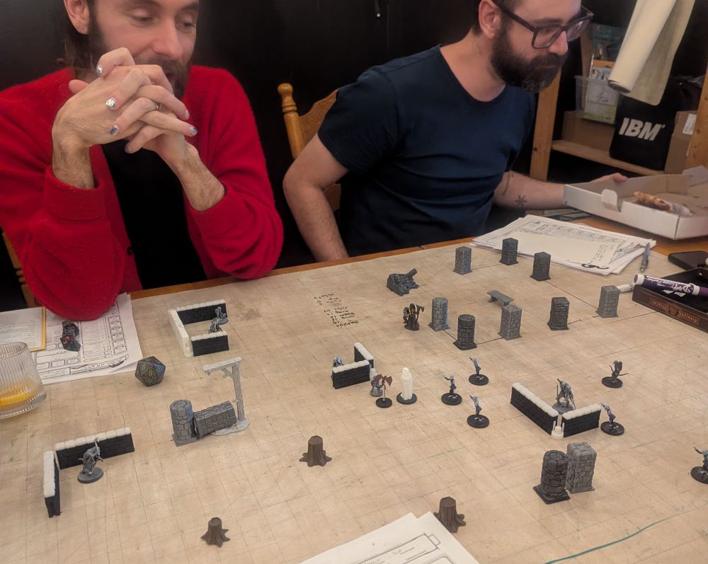 Elio and Phil sit in front of a rolled out DND map as their characters face near death.